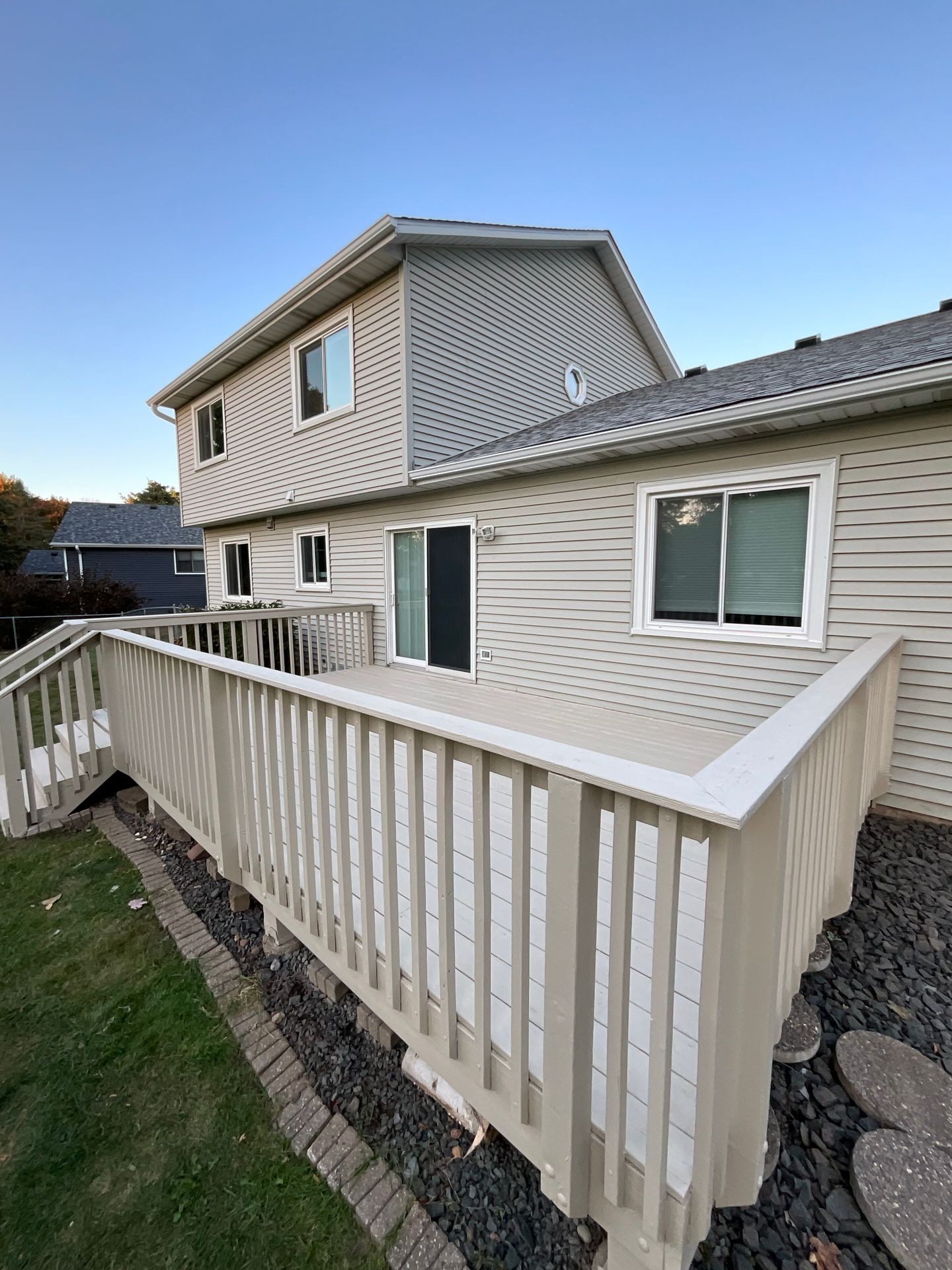 Backyard view of a two-story house with a beige wooden deck and railing.